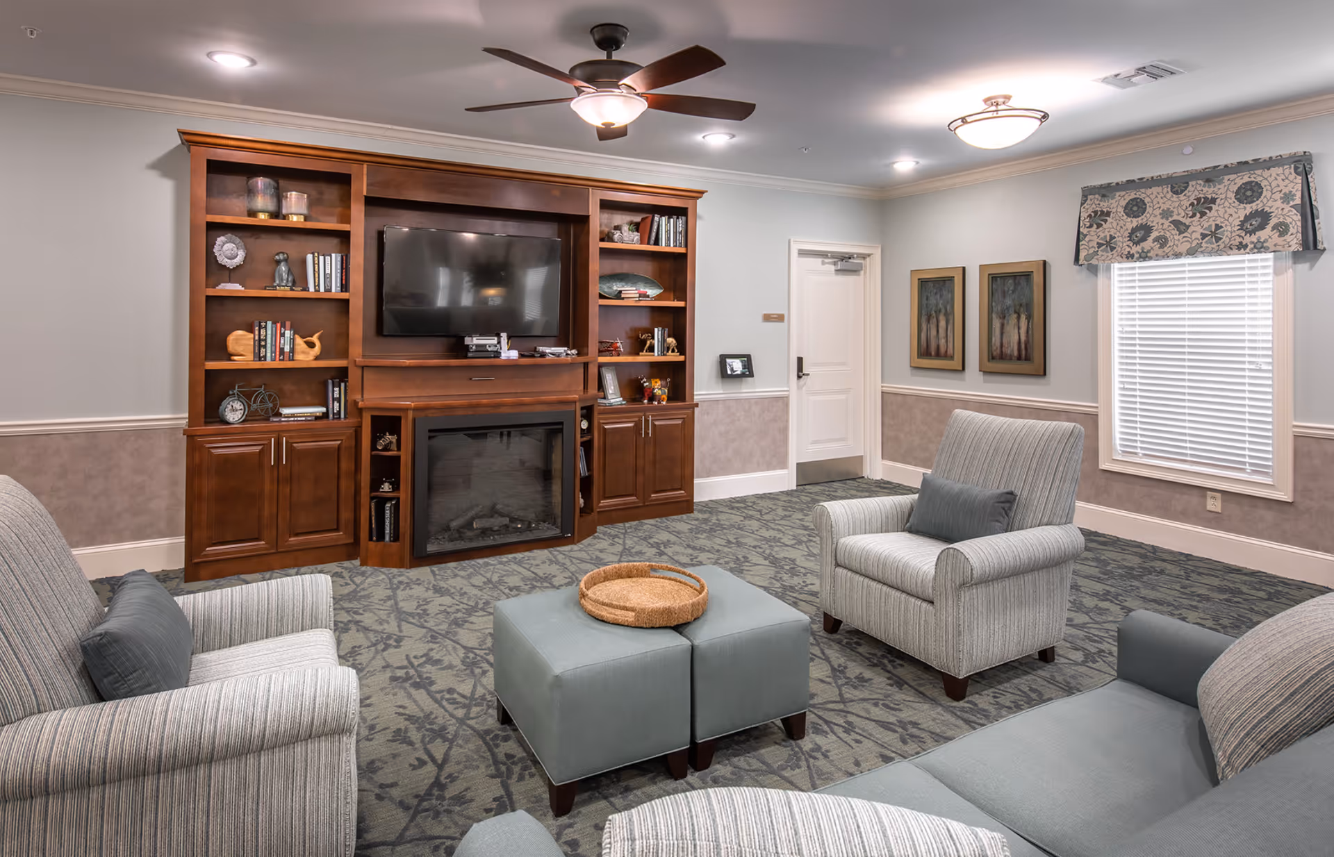 Cozy sitting room with upholstered chairs, ottomans, and a large wooden entertainment center holding a TV and fireplace.