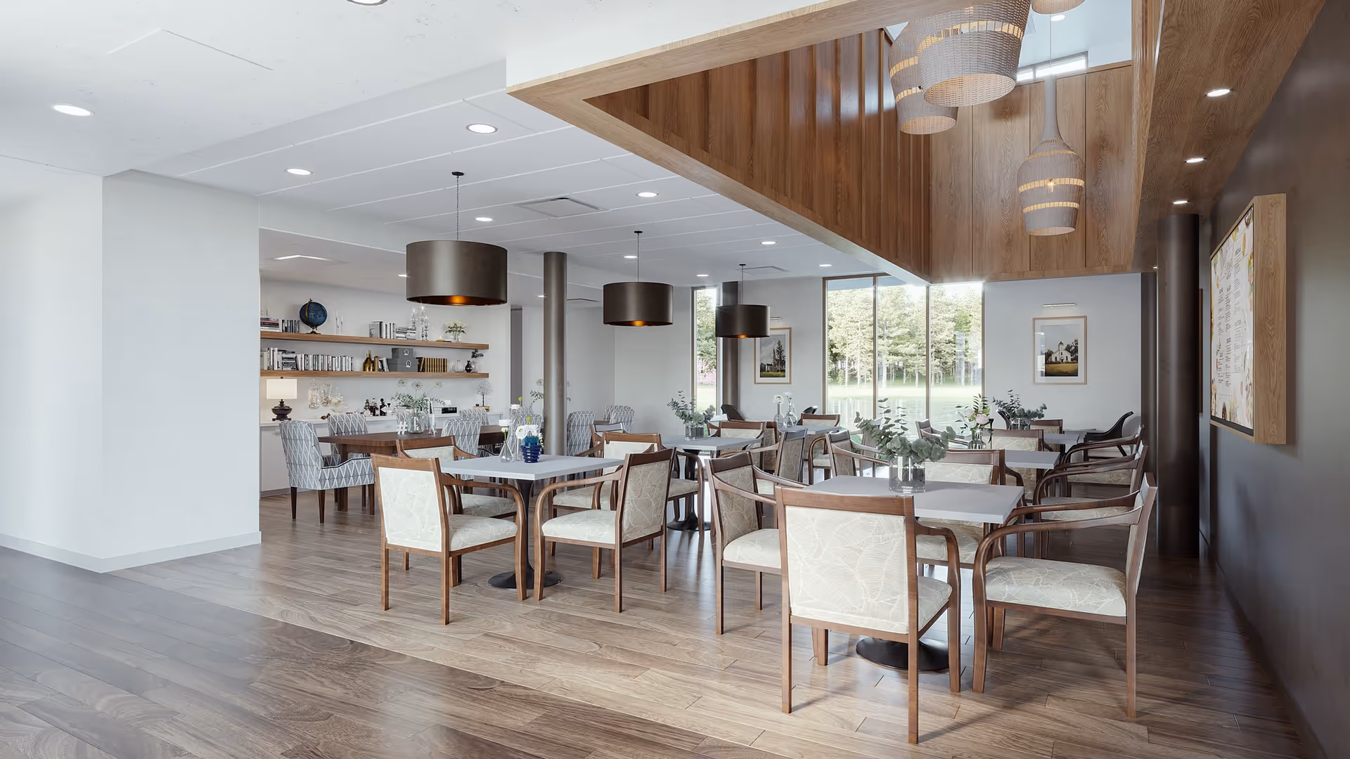 Bright communal dining room with wooden tables and upholstered chairs, pendant lights, and large windows overlooking greenery.