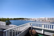 View from a balcony overlooking a body of water with boats docked at a marina and a large multi-story building in the background under a clear blue sky.