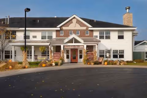 Two-story senior living facility exterior with pumpkins and fall decorations around the entrance.