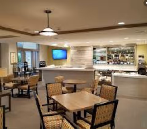 Well-lit communal dining area with several tables and chairs and a service counter/bar in the background.