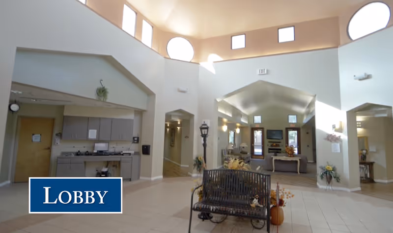 Spacious, sunlit lobby with high ceilings, seating bench, and reception area in a senior living facility.