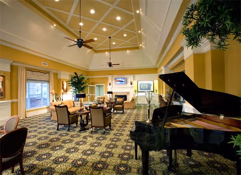 Spacious elegant common room with a grand piano, multiple seating areas, a fireplace, and a coffered ceiling.