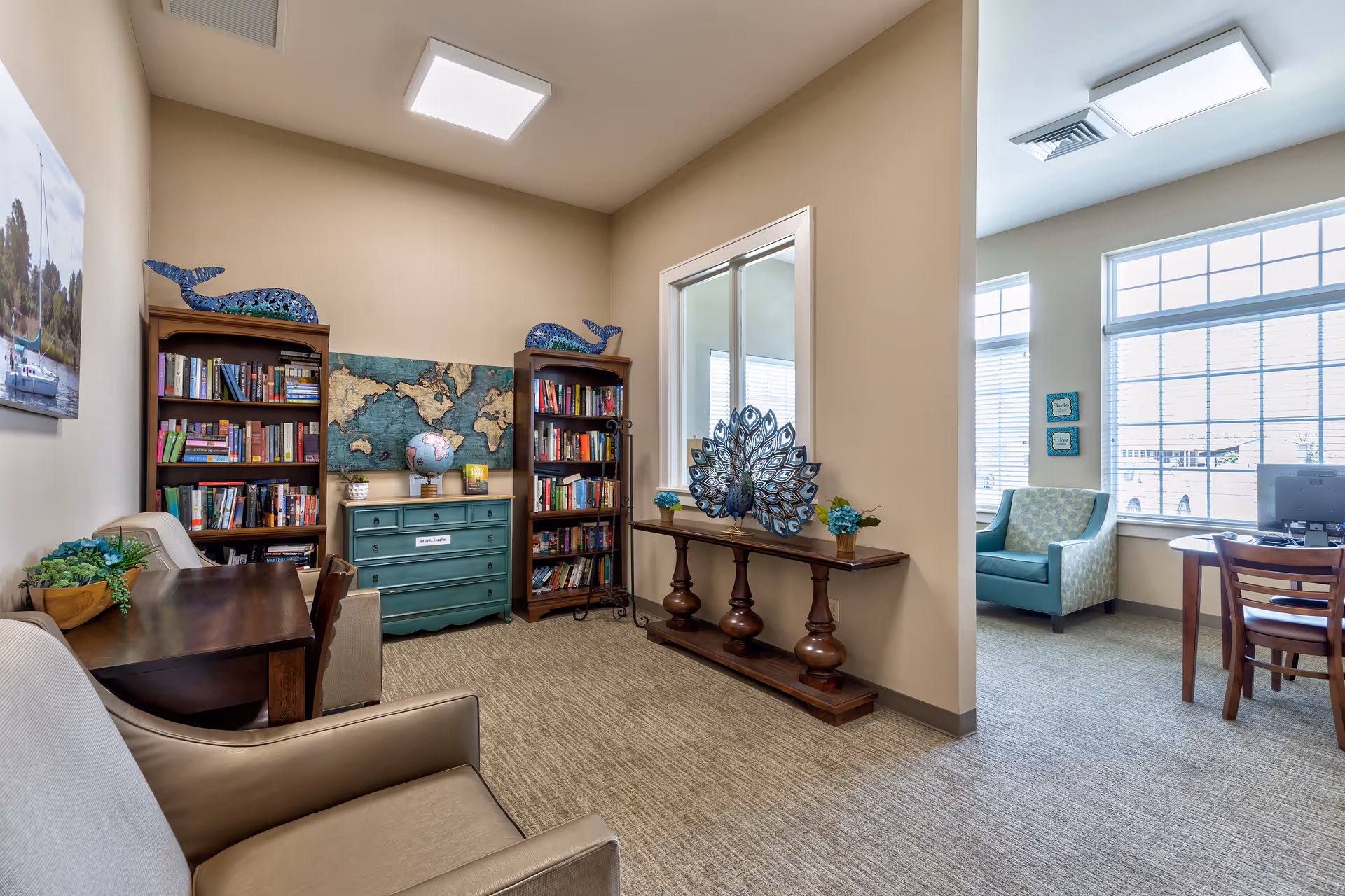 Comfortable common room with bookshelves, seating, a decorative console table and a desk by large windows.