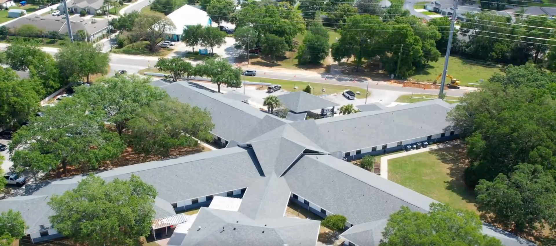 Aerial view of a senior living facility named Gardens of Westbrooke showing a large building with multiple wings surrounded by trees, parking areas, and nearby roads.