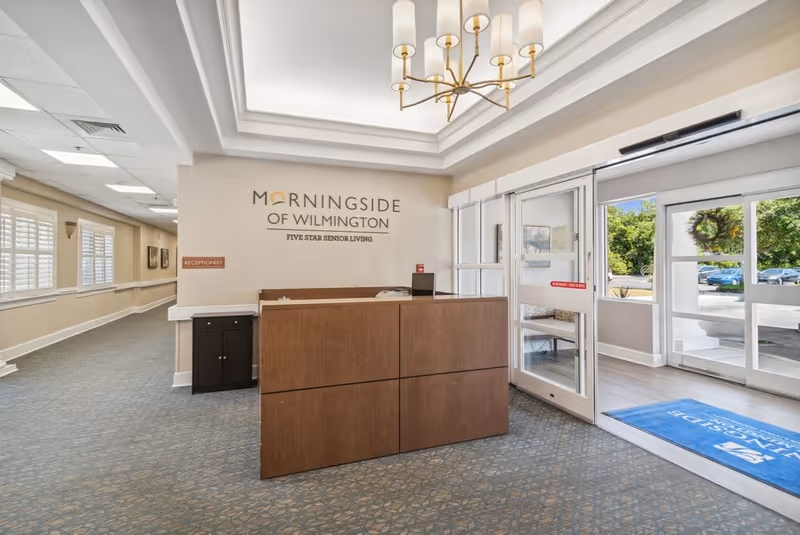 Reception desk and entry foyer of Morningside of Wilmington senior living facility with signage on the wall and glass doors to the outside.