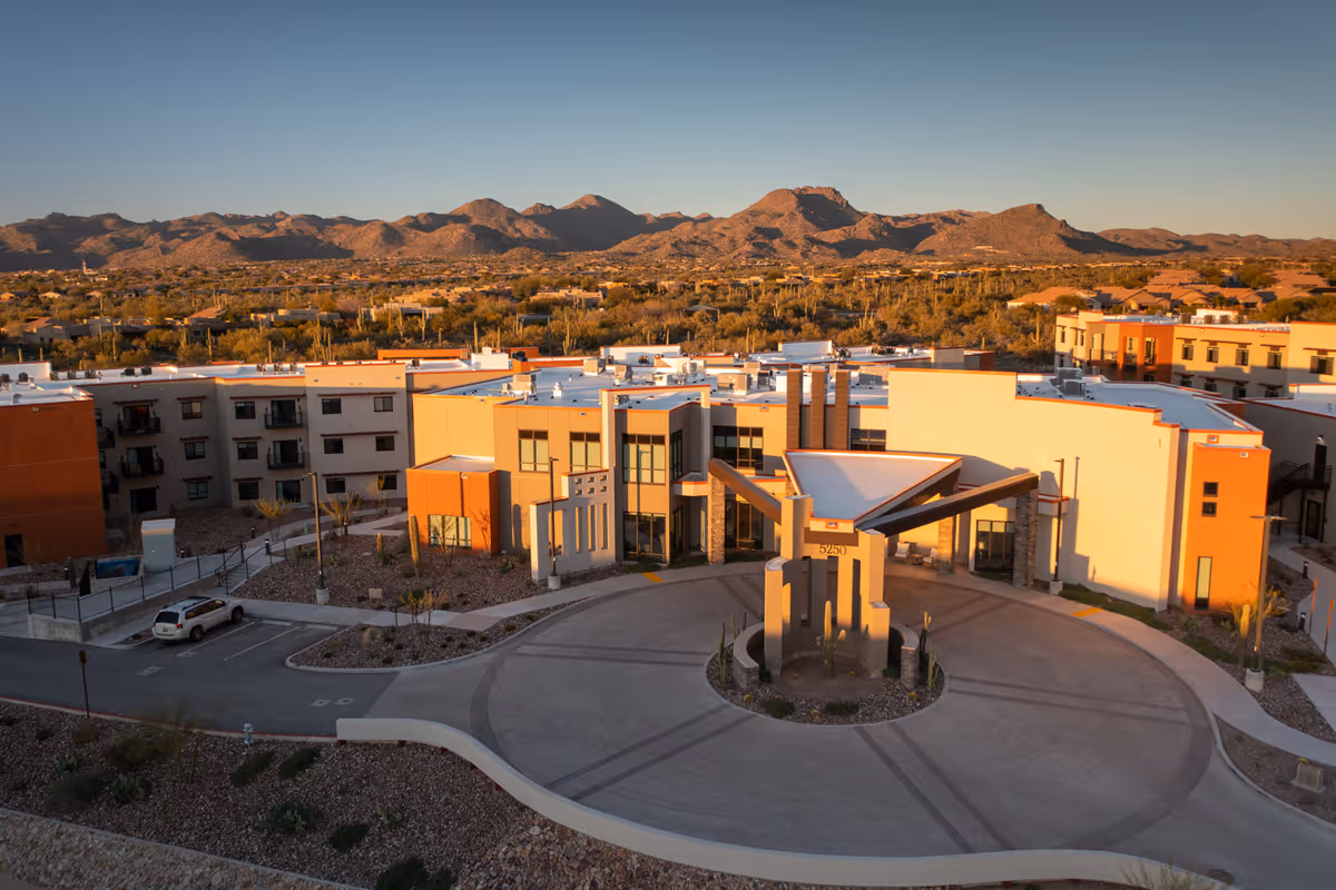 Aerial view of La Sonora at Dove Mountain senior living facility with a circular driveway and modern building architecture, set against a backdrop of desert landscape and mountains under a clear sky.