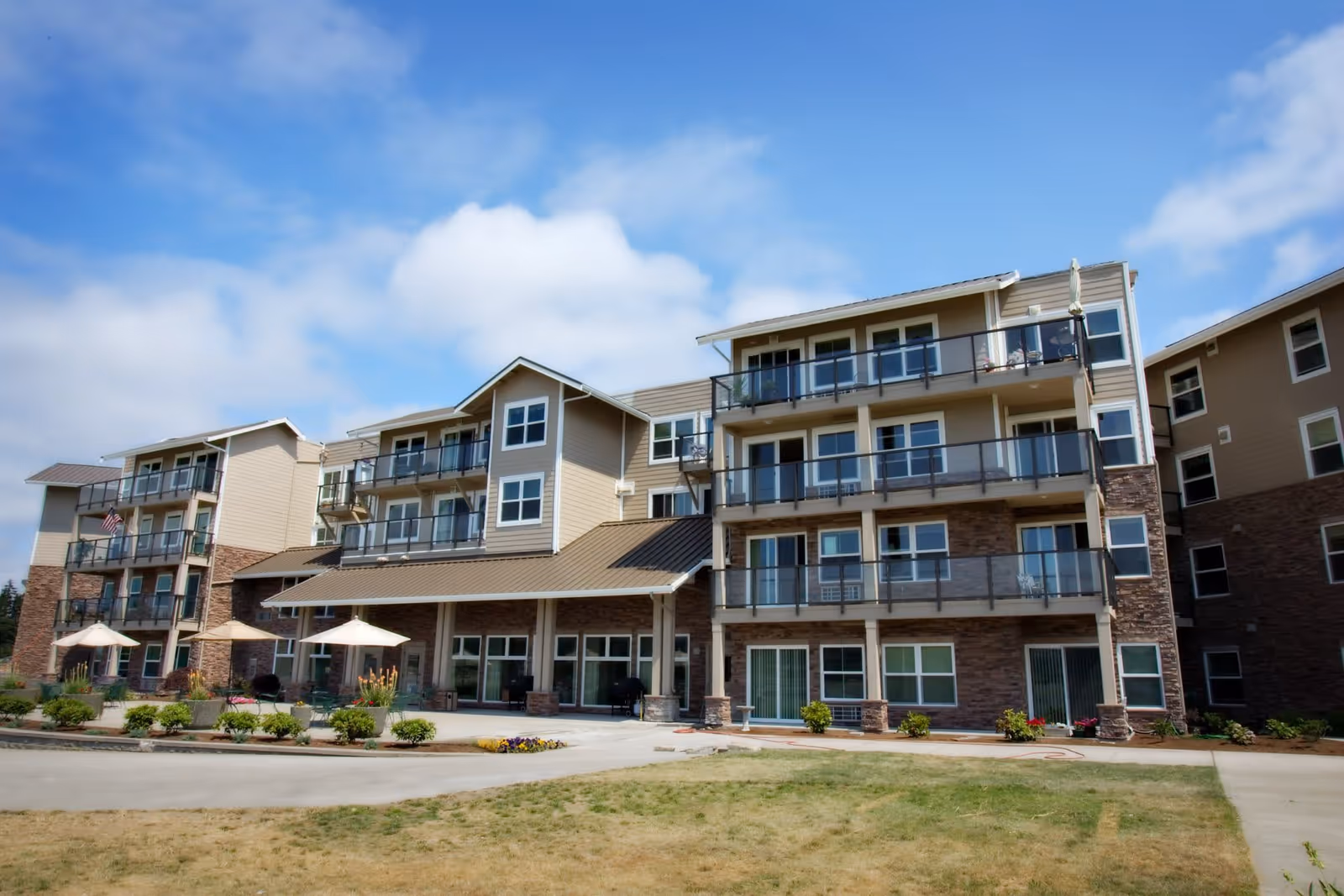 Exterior view of Crista Shores building featuring multiple balconies, a landscaped entrance with umbrellas, and a clear blue sky.