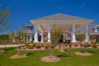 A columned entrance pavilion with landscaped lawn and young trees in front of the facility.