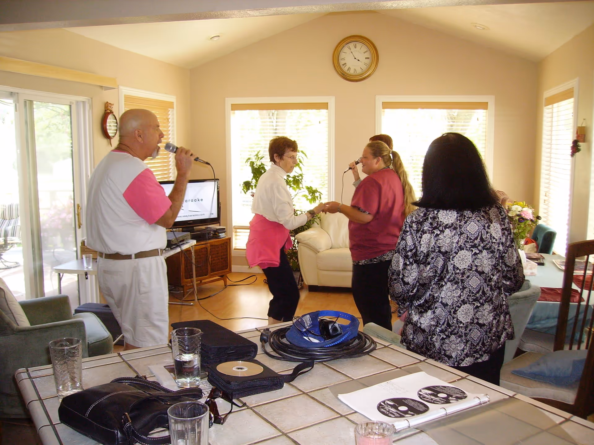 Several people singing karaoke and socializing in a bright living room.