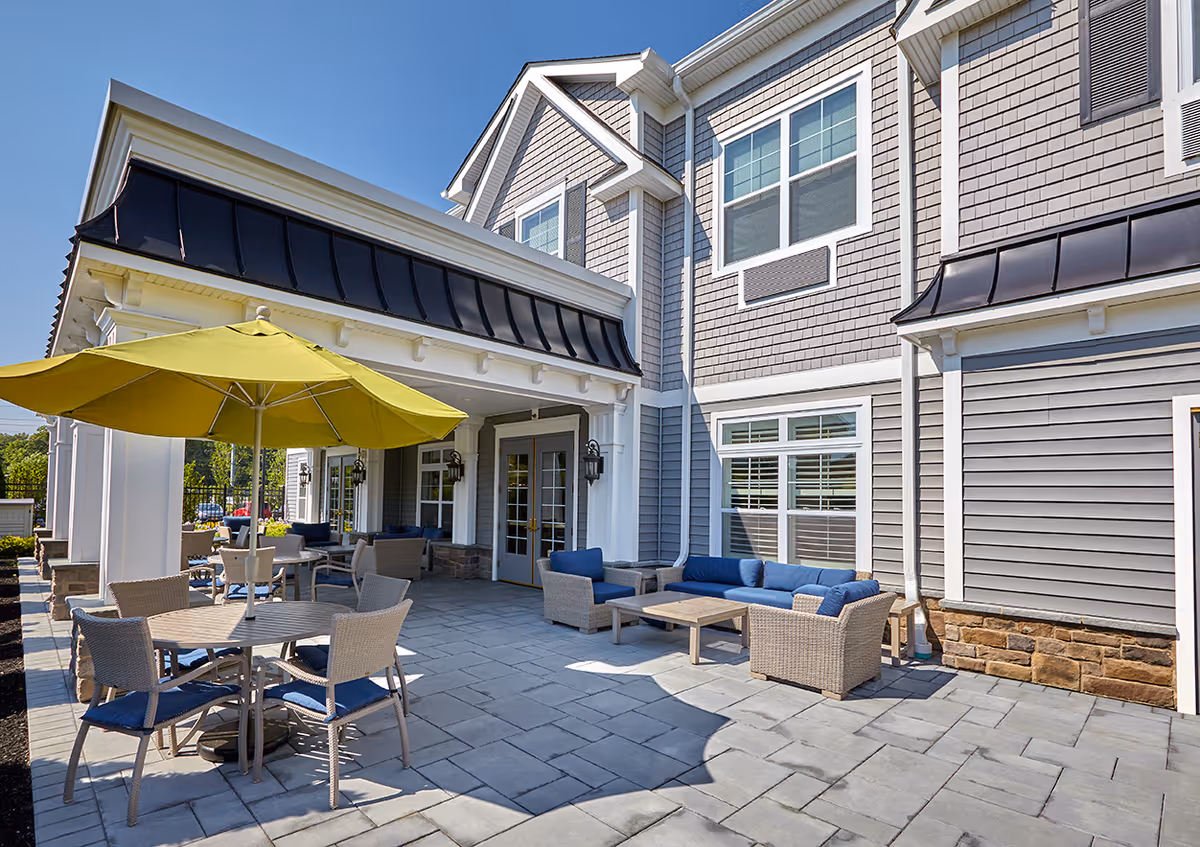 Outdoor patio with tables, chairs, a yellow umbrella and lounge seating in front of a gray shingled building.