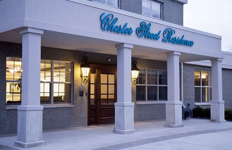 Front entrance of Chester Street Residence with columns, a script sign, lanterns, windows, and a wooden double door.