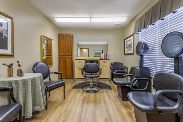 A small salon room with styling chairs, hooded hair dryers, a vanity mirror and several waiting chairs.