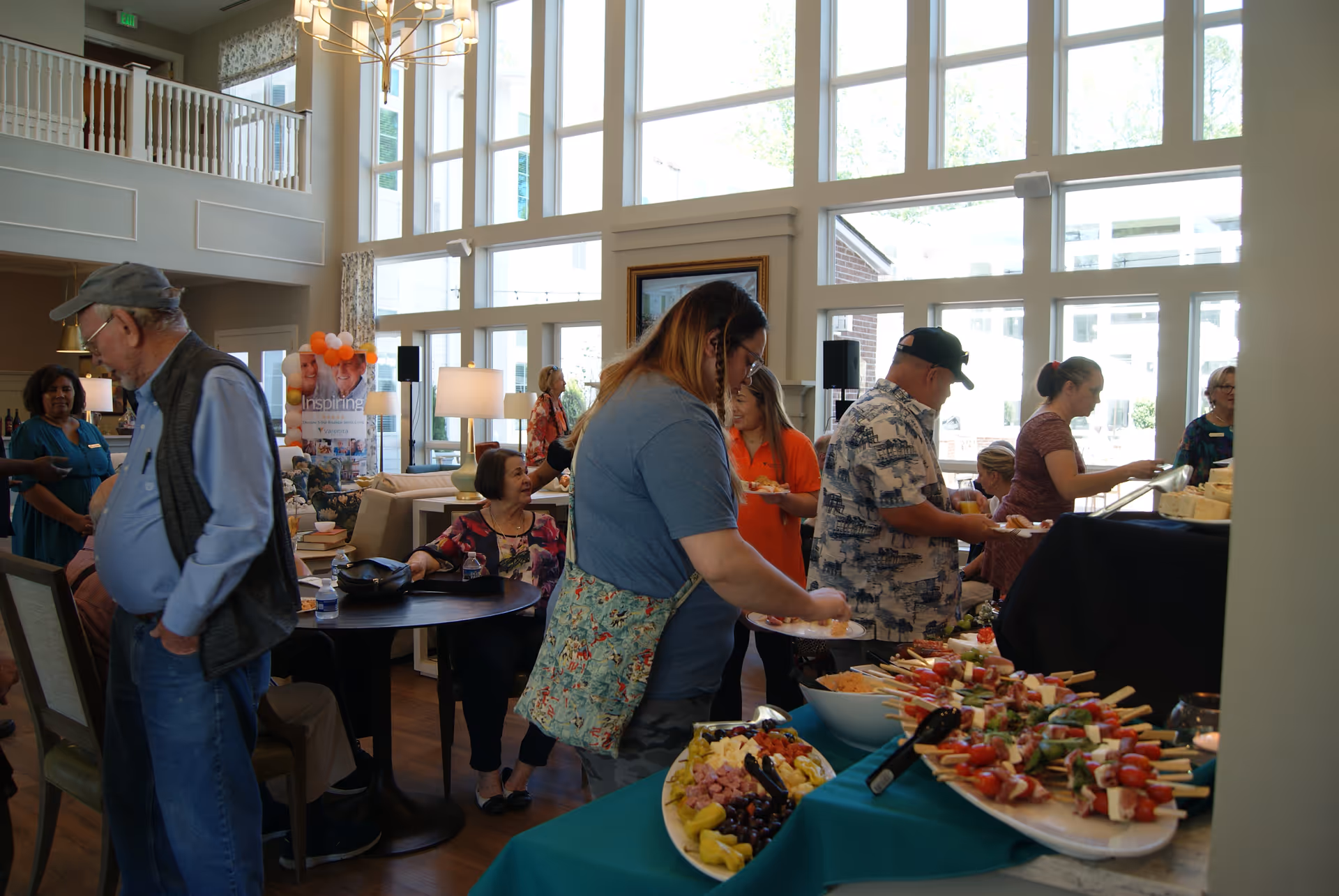 Residents and guests serve themselves from a buffet in a bright senior living common room with large windows.