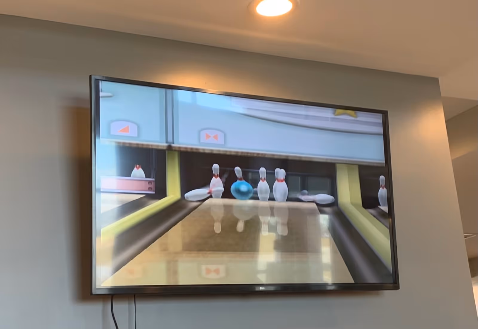 A flat-screen LG television mounted on a wall displaying a virtual bowling game with bowling pins and a blue bowling ball on a lane.