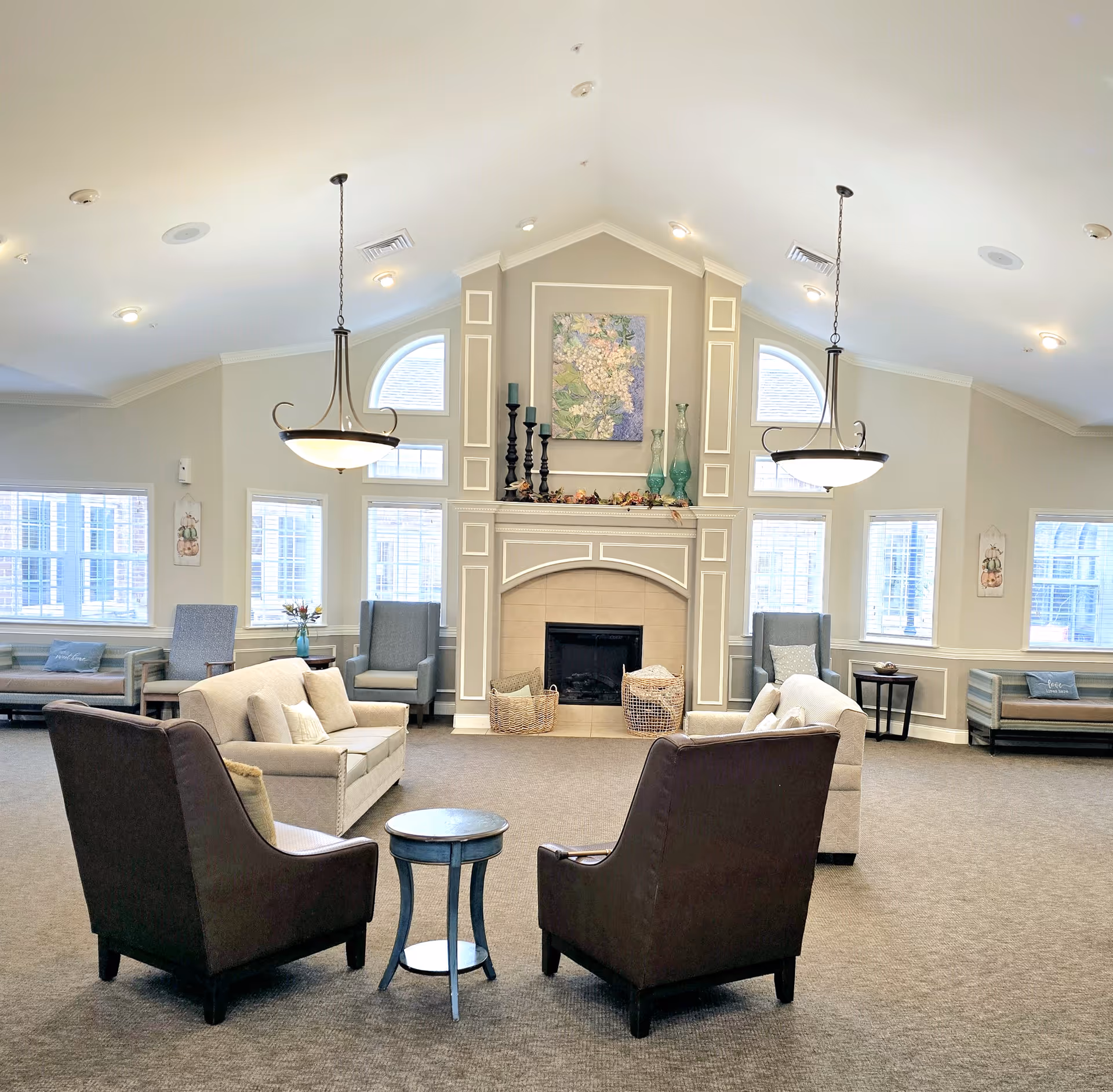 Spacious senior living common room with seating arranged around a central fireplace and decorative pendant lights.