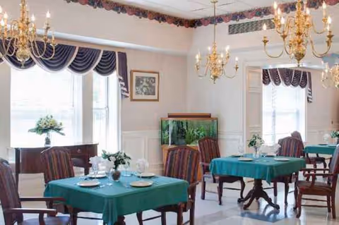 Elegant dining room with teal tablecloths, chandeliers, and large windows in a senior living facility.