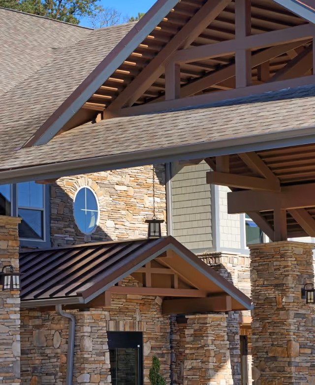 Stone-clad entrance with multiple gabled roofs, exposed wooden beams, lanterns, and a round window on the façade.