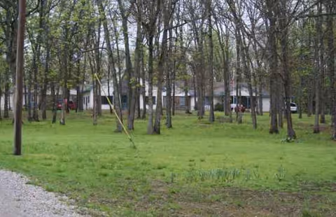 Grassy outdoor area with many trees and a building in the background.