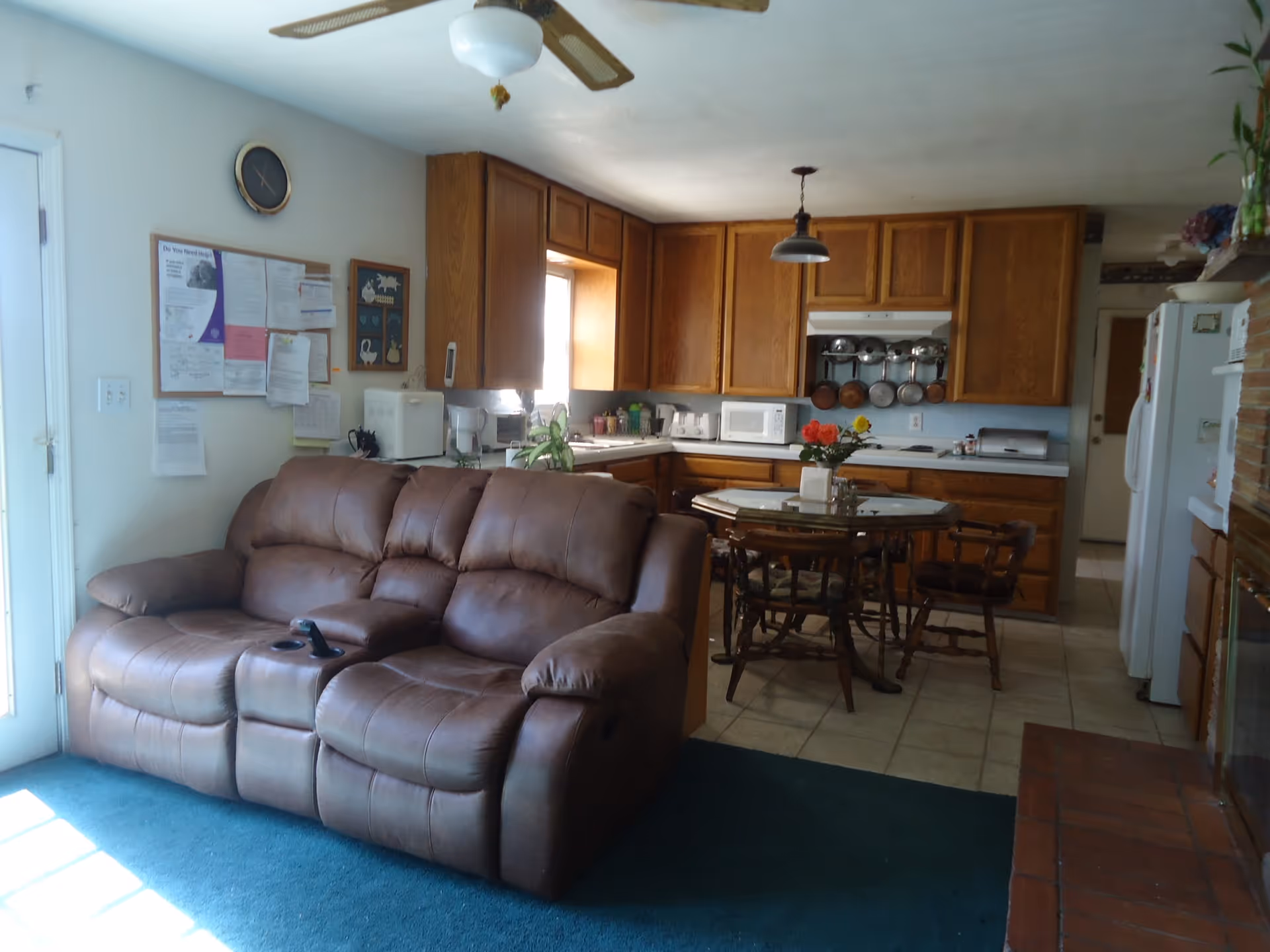 Cozy open-plan living room and kitchen with a brown leather sofa, dining table, and wooden cabinets.