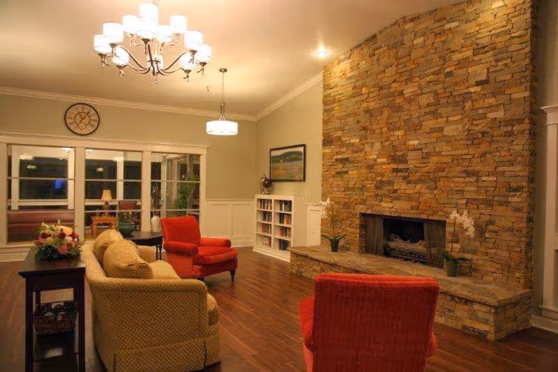 Cozy communal lounge with sofas and armchairs facing a large stone fireplace and hardwood floors.