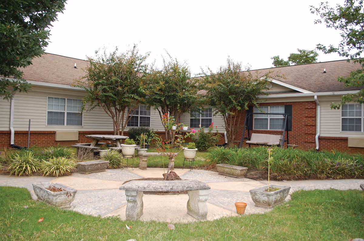 Courtyard with stone benches, planters, a picnic table and landscaping in front of a single-story brick-and-siding building.