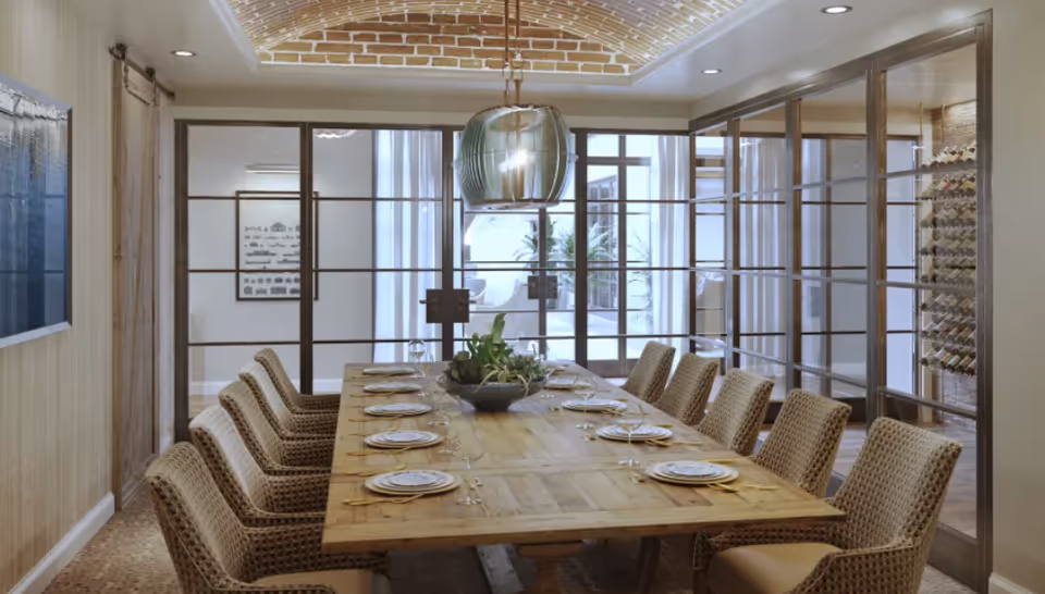 Long wooden dining table set with place settings and woven chairs under a pendant light in an elegant dining room with glass partition walls.