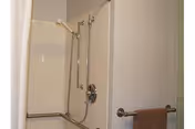 Accessible shower stall with grab bars, a handheld shower head, and a towel hanging on a wall-mounted bar.