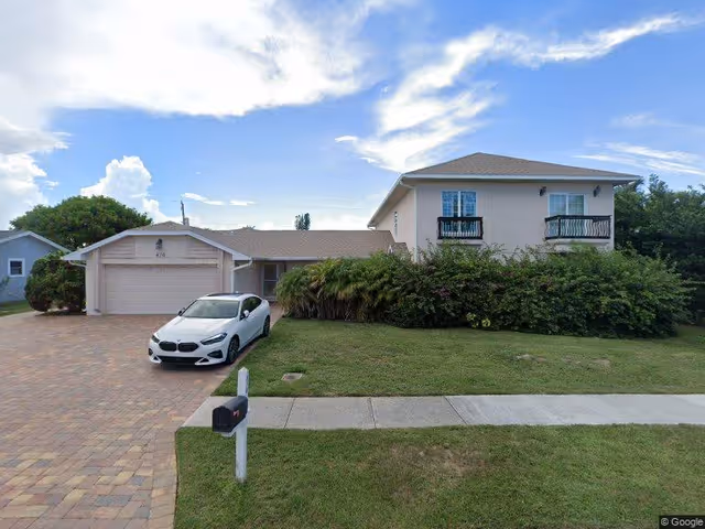 Two-story residential building with an attached garage, driveway with a white car, and front lawn under a partly cloudy sky.