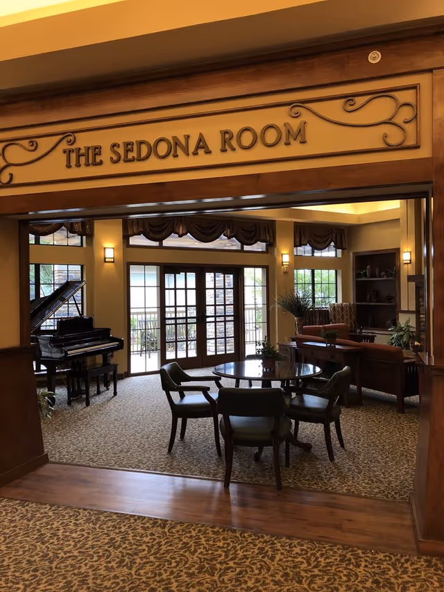 Entrance to "The Sedona Room," a furnished lounge with a round table and chairs, piano and seating area in front of large glass doors.