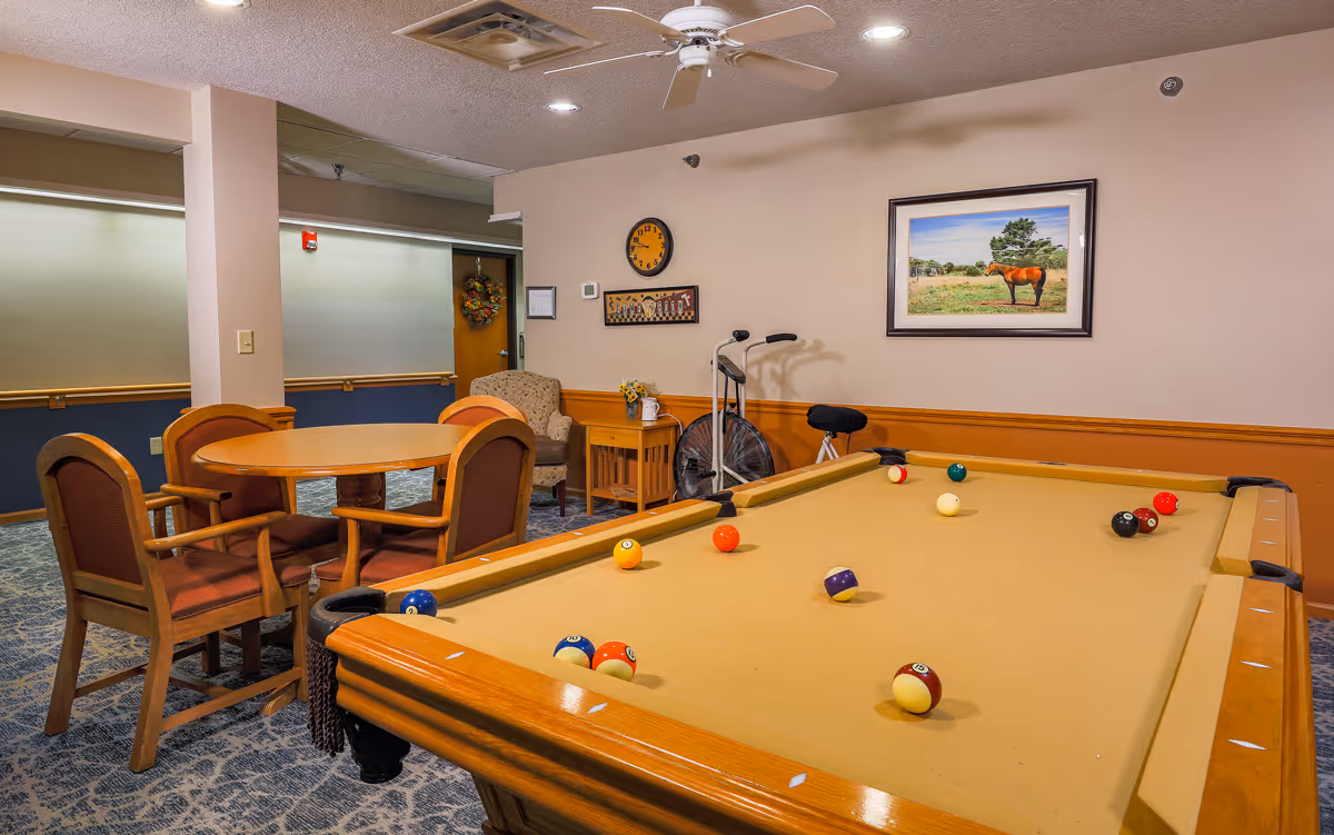 Recreation room with a pool table, a round table and chairs, and framed artwork on the wall.