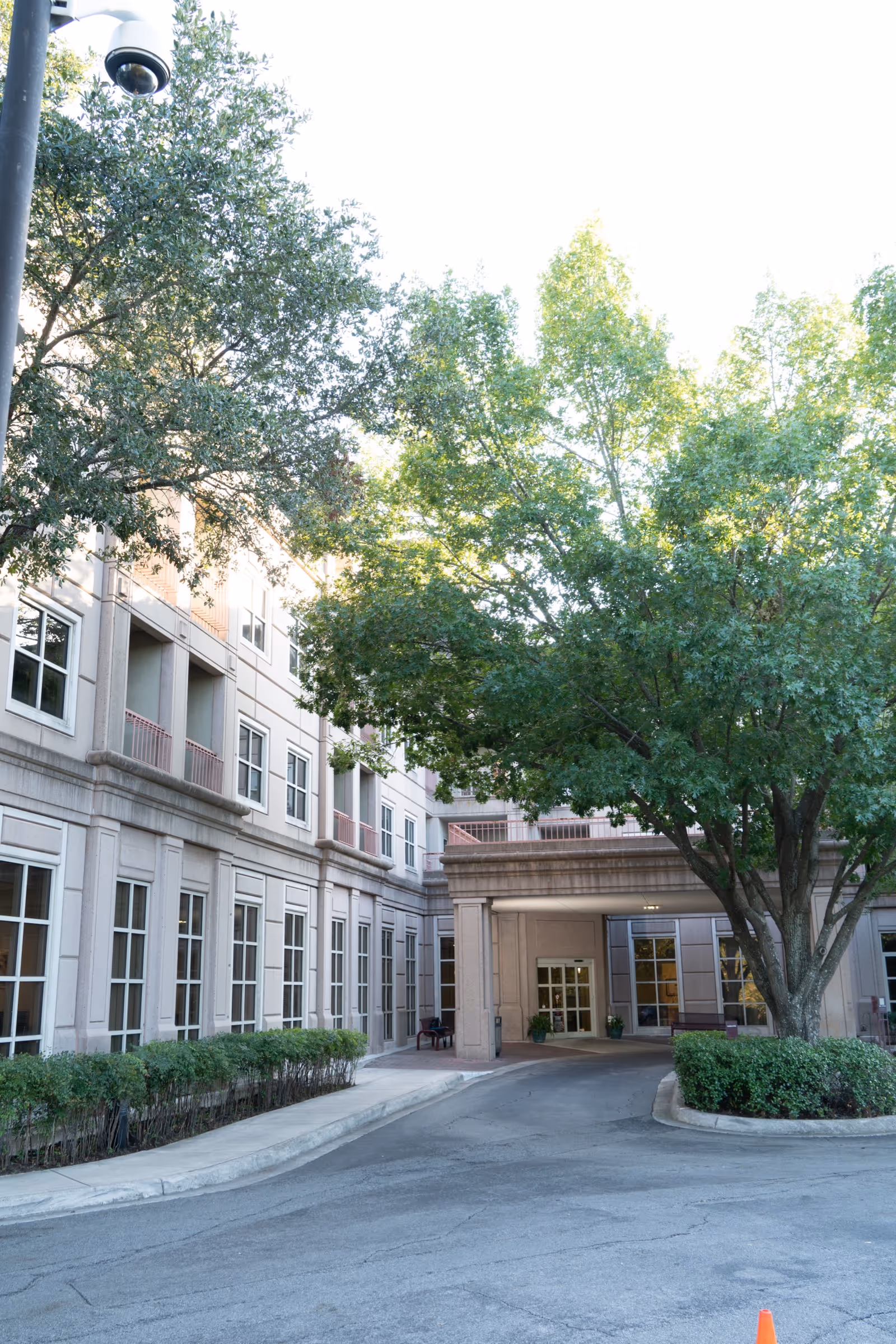 Exterior view of Parklane West Healthcare Center showing the building's entrance with large windows, a covered drop-off area, and surrounding greenery including trees and bushes.
