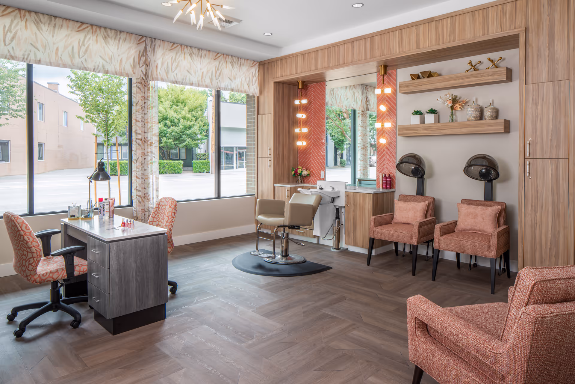Bright, modern salon area with styling chairs, a manicure table, hooded hair dryers and large windows in a senior living facility.