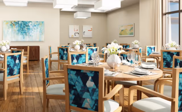 Bright dining room with round wooden tables set with place settings and wooden chairs featuring teal patterned upholstery.