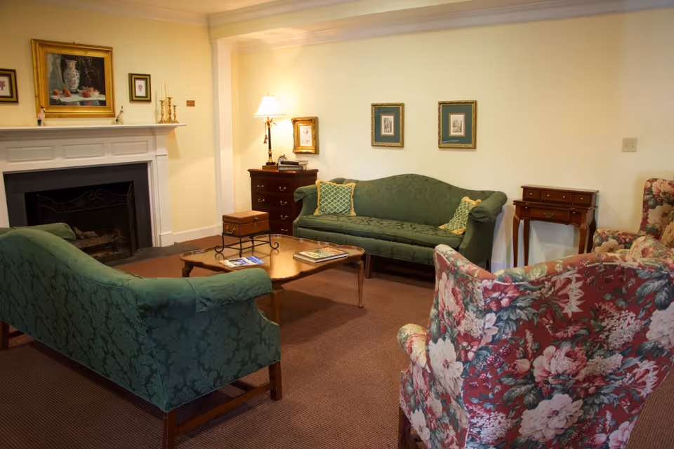 Traditional sitting area with green upholstered sofas, floral armchairs, a coffee table, and a fireplace.