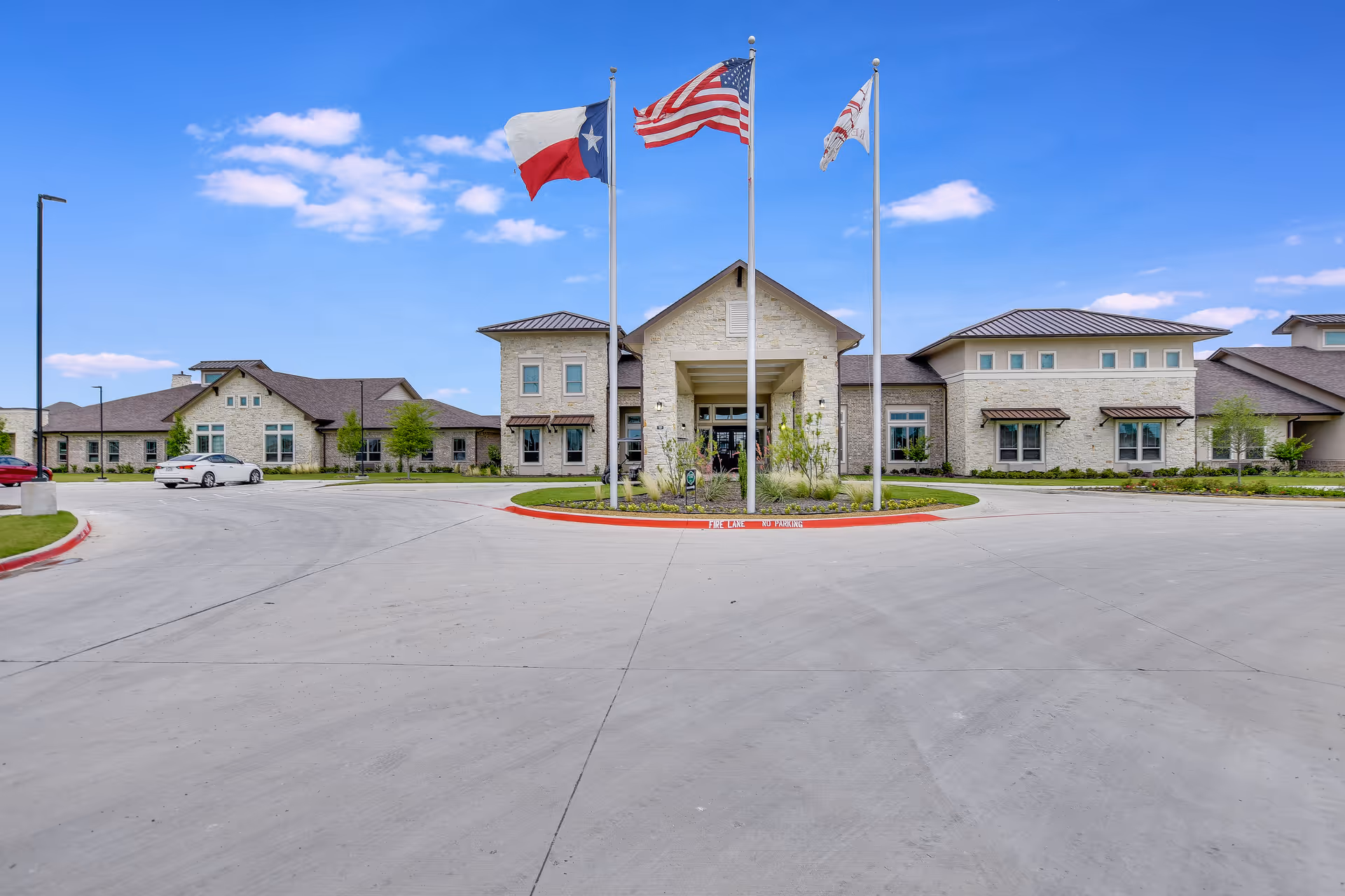 Front exterior view of Arabella of Red Oak Senior Living with flagpoles and driveway.