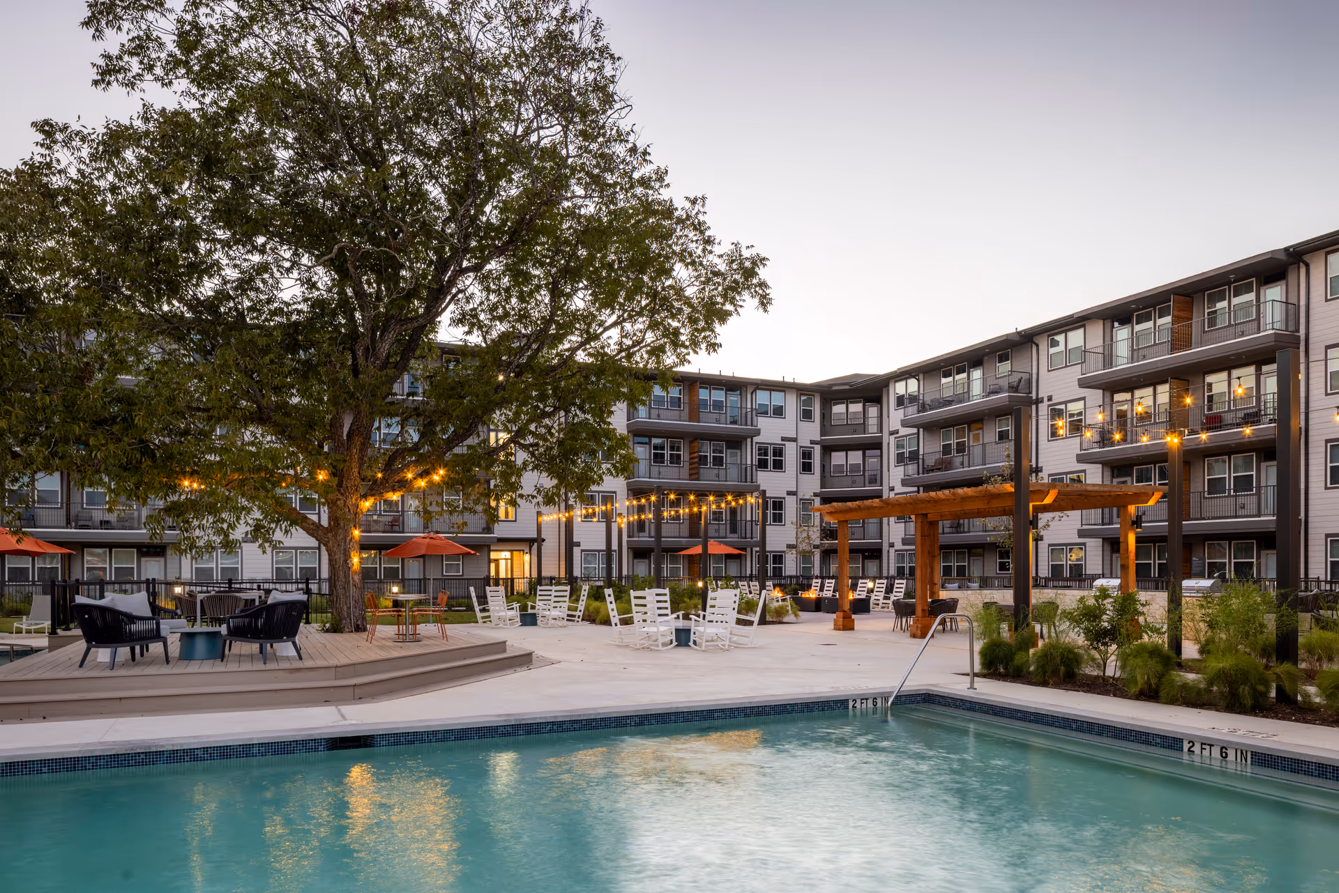 A courtyard pool area with lounge chairs, string lights, and multi-story resident apartments.