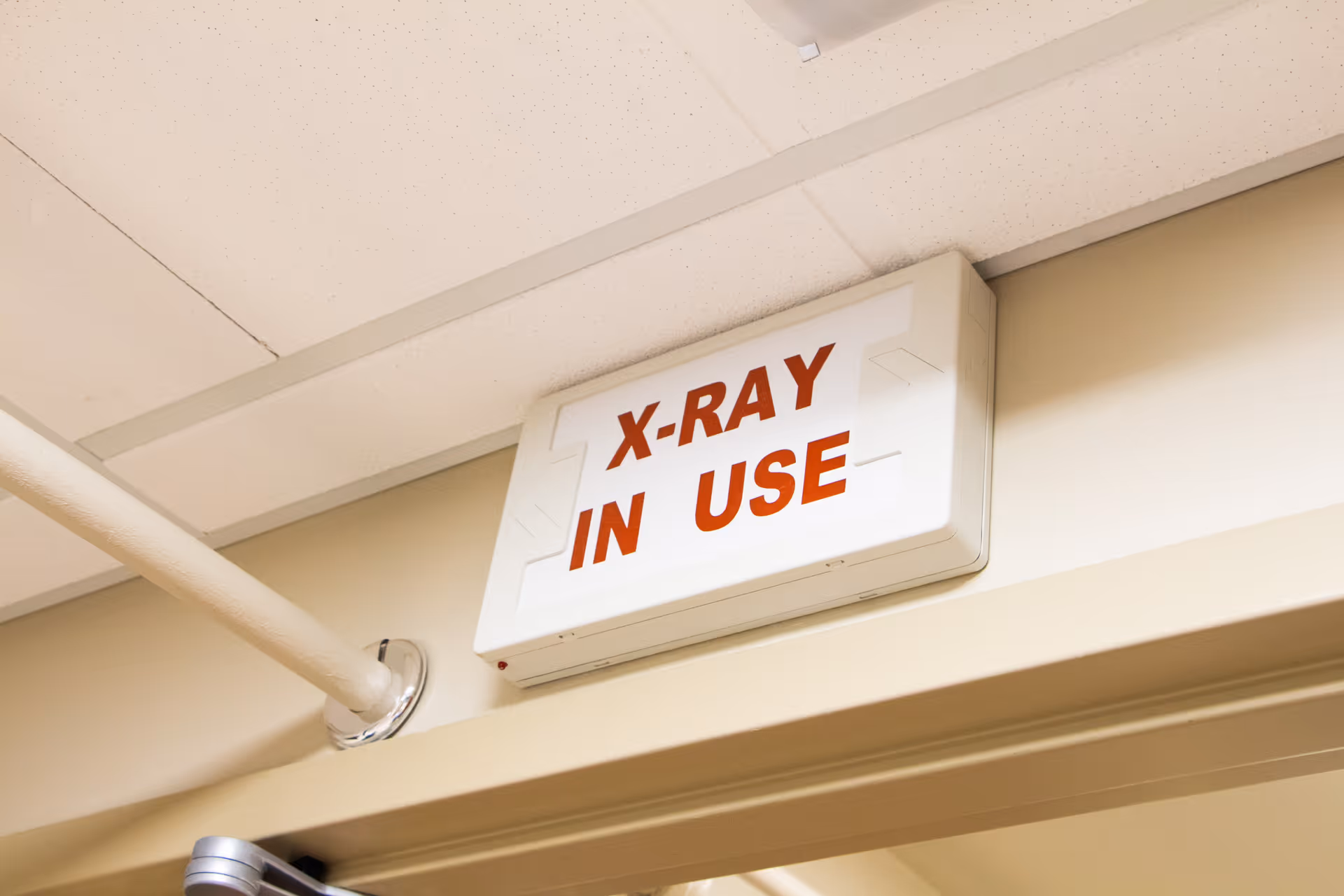A rectangular white sign with red text reading 'X-RAY IN USE' mounted above a doorway in a medical facility.