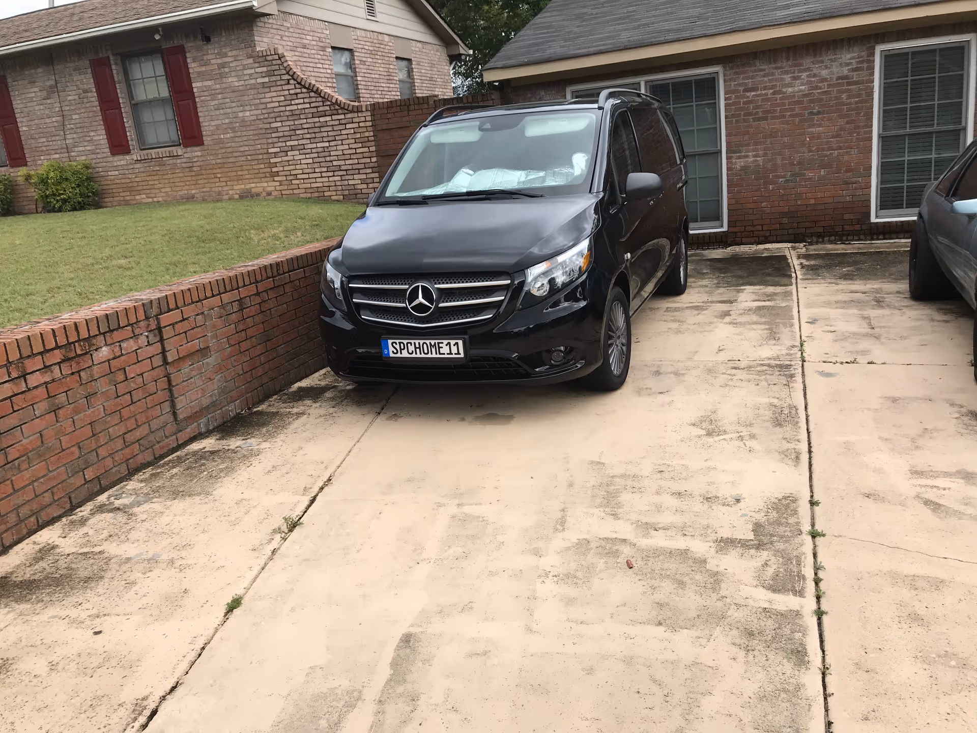A black Mercedes-Benz van parked in a driveway next to a brick house with red shutters and green lawn.