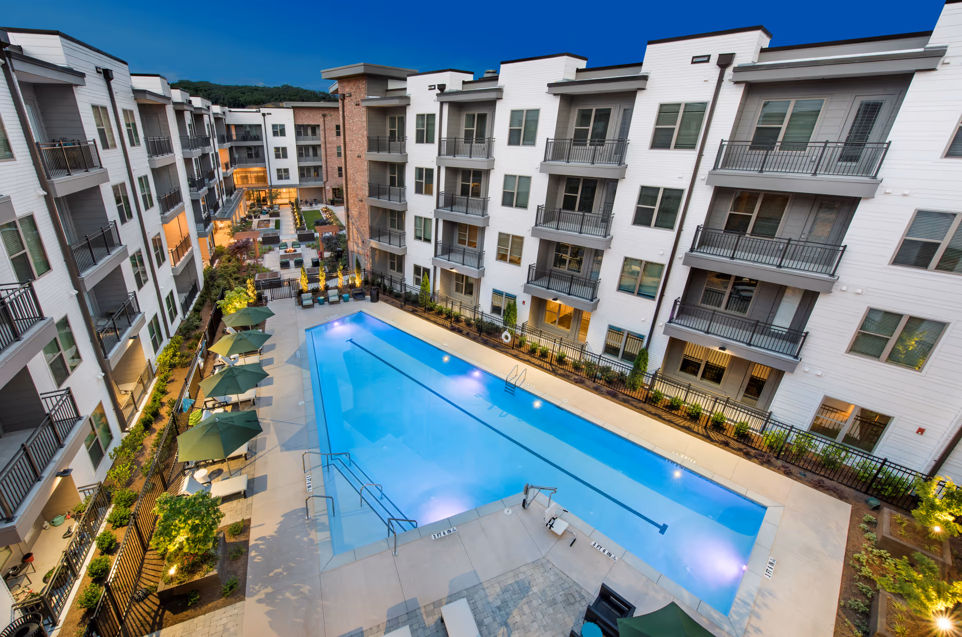 Aerial view of a central outdoor swimming pool in a courtyard surrounded by multi-story apartment balconies and patio seating.