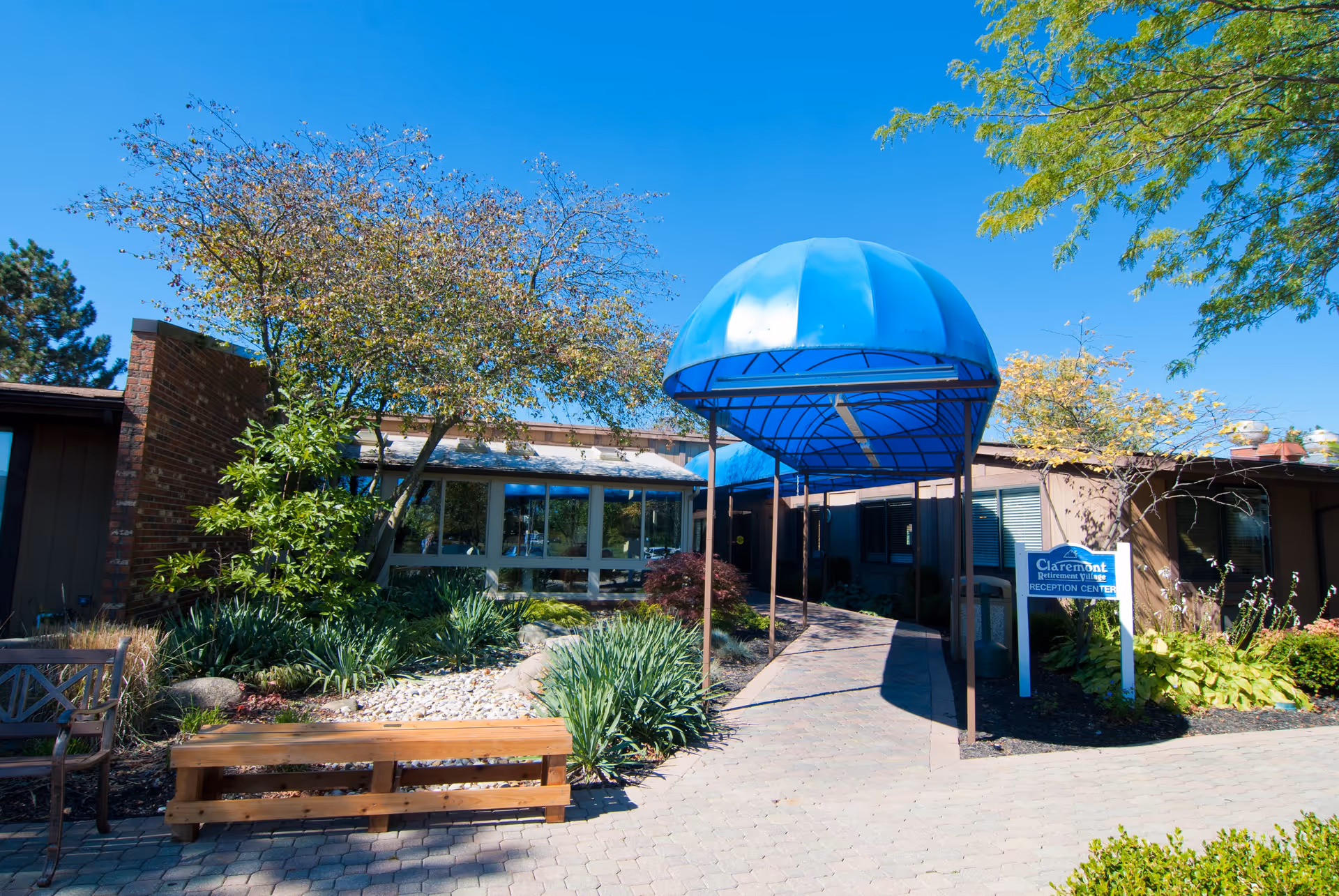 Entrance of Claremont Retirement Village with a blue canopy over a walkway, landscaped courtyard and benches.