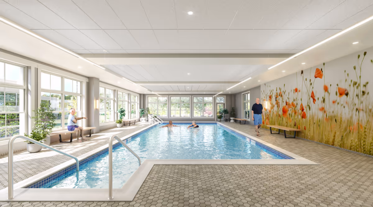 Bright indoor community pool with large windows, benches and plants, and a few people using the pool area.