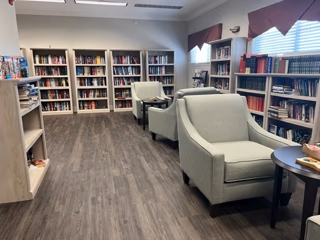 Quiet interior reading room with bookshelves lining the walls and upholstered armchairs arranged around small tables.