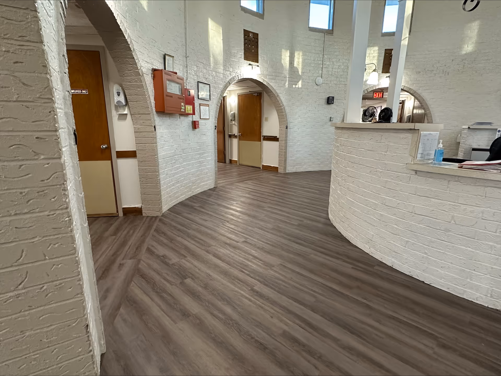 Curved white-brick reception desk and arched doorways in a nursing facility lobby with wood-look flooring.