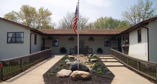 Front entrance courtyard of Hoover Haus with a central flagpole, rock garden, and ramps leading to the single-story building.