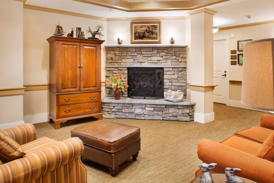 Cozy seating area with armchairs, ottoman, wooden armoire and stone fireplace in a lounge.