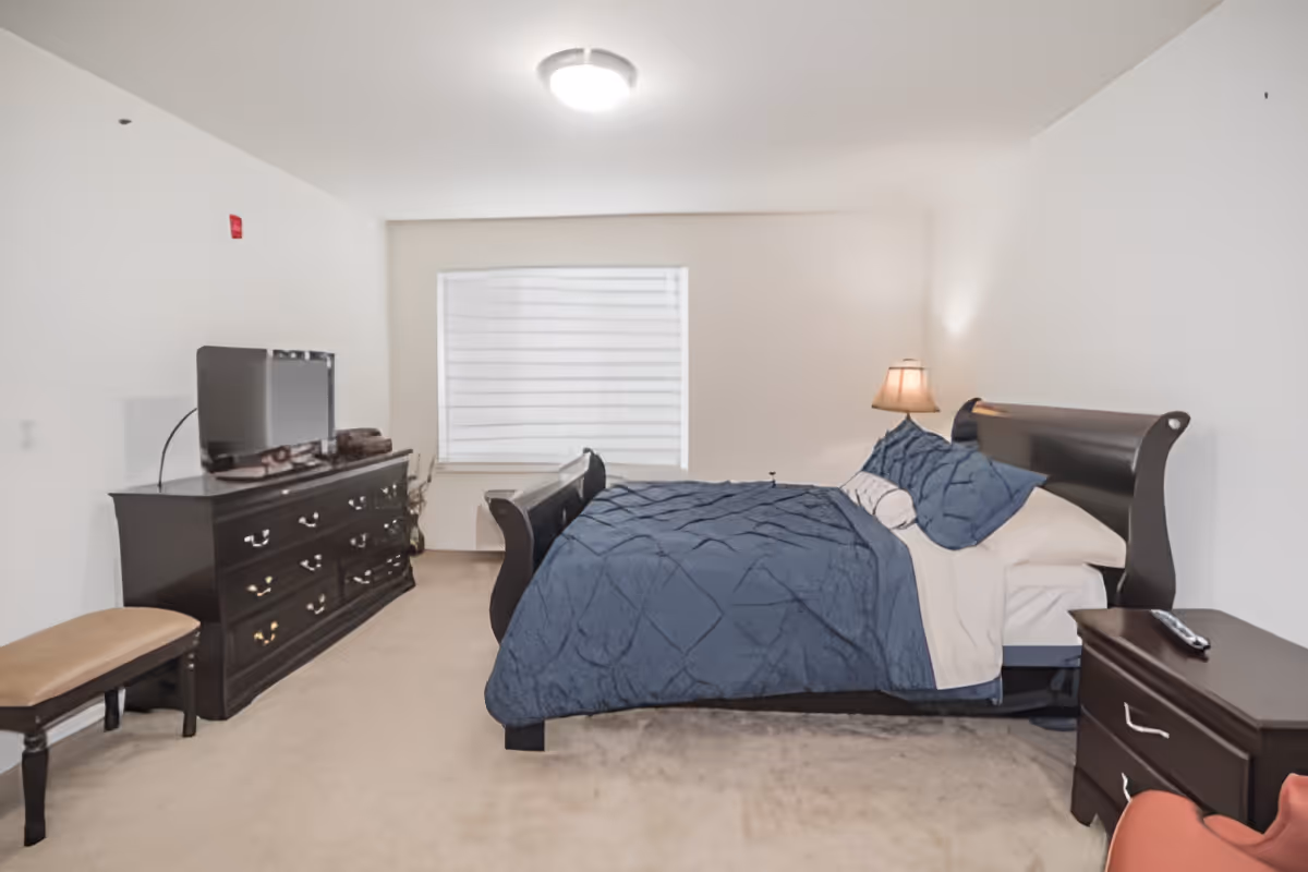 A furnished bedroom with a dark wooden sleigh bed dressed in blue bedding, matching dressers, a TV, and a window.