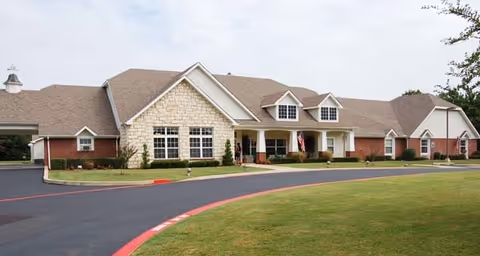 Front exterior of a single-story senior living facility with brick and stone facade, covered entrance, and circular driveway.