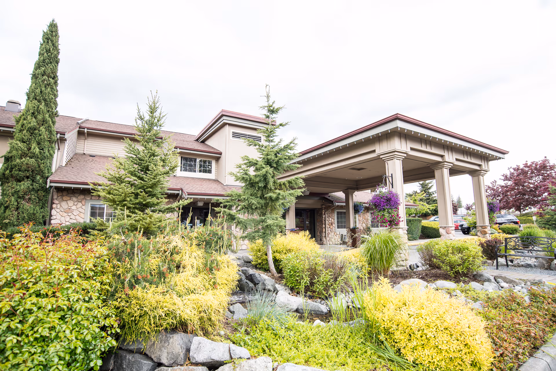 Front entrance of a senior living facility with a covered porte-cochère and landscaped gardens.