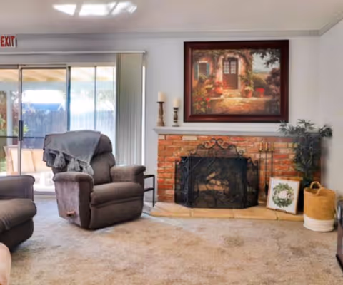 Carpeted living room with two recliners, a brick fireplace with decorative screen and framed painting above, and sliding glass doors to a patio.